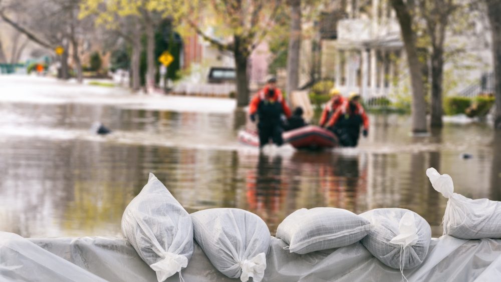 Flood protection sandbags with flodded homes in background. People in rescue boat in city