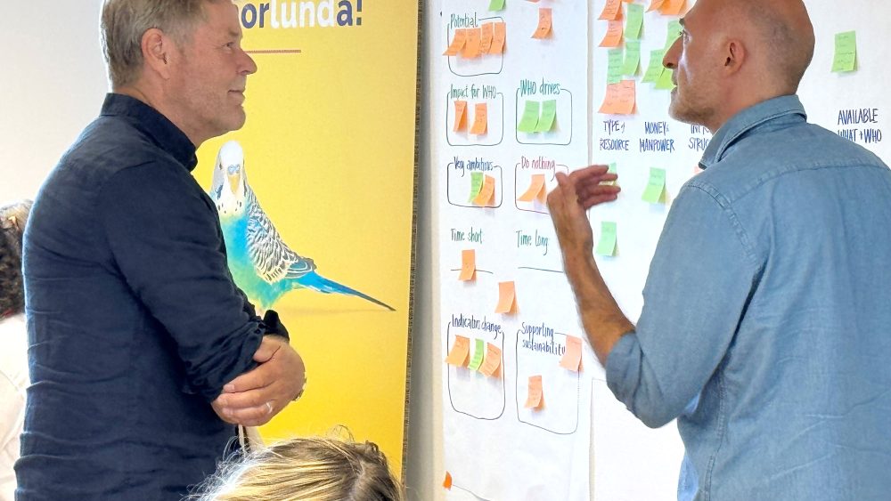Two men in front of a board with post-it notes discussing