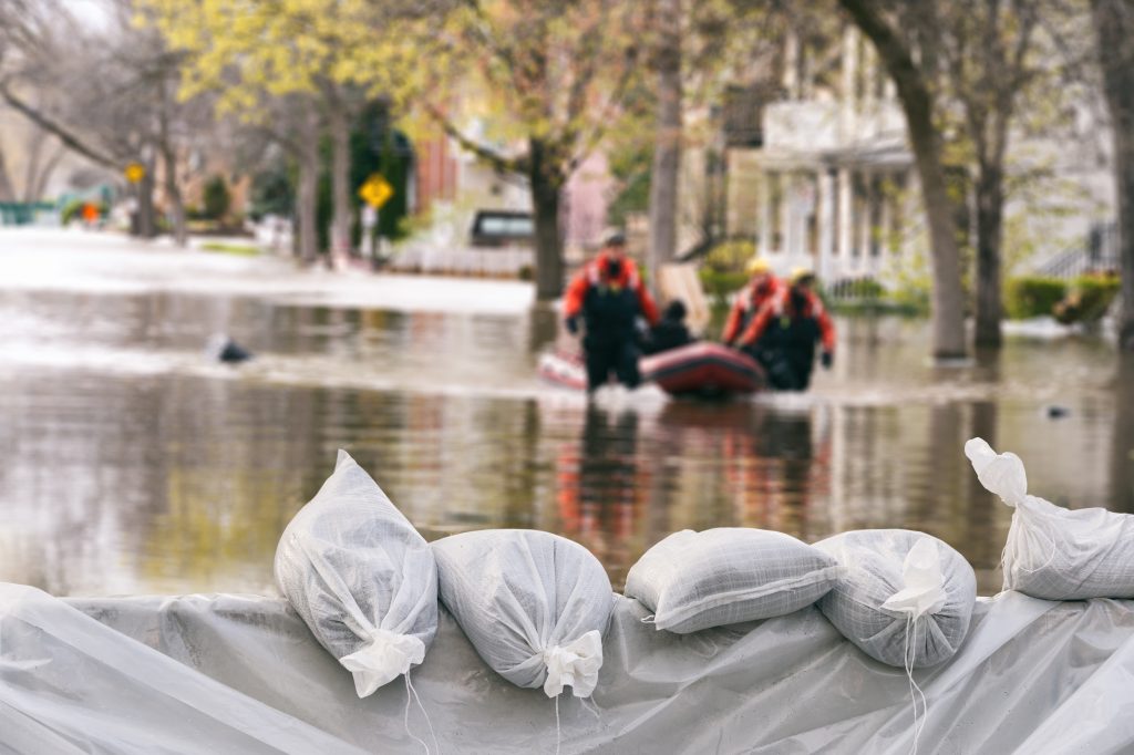 Flood protection sandbags with flodded homes in background. People in rescue boat in city